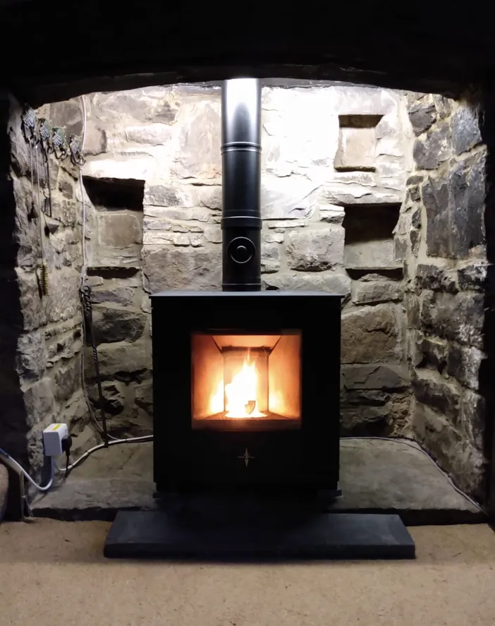 Pellet stove installed in a stone fireplace recess with visible flue.